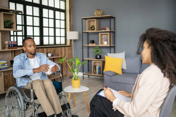 Handicapped man is sitting in a wheelchair for a therapy session with a female psychiatrist in a comfortable mental health meeting room