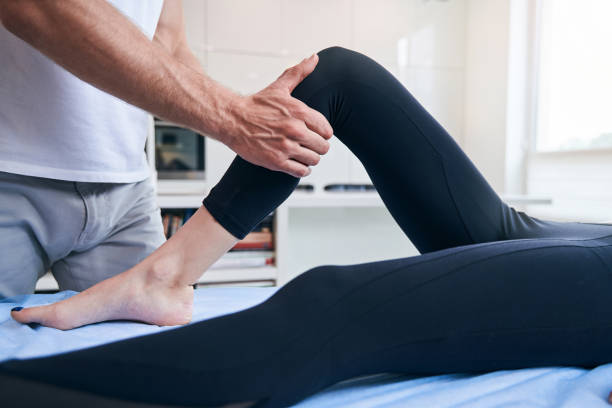 Cropped head side view portrait of unrecognized man physiotherapist stretching woman leg in medical office