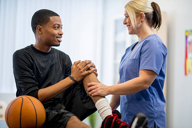 A male teenage basketball player is at the doctors office to have some work done on his injury. A physical therapist is working with him on his injury.