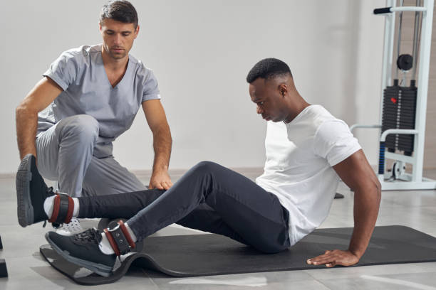 Focused patient rolling foam roller along underside of lower leg assisted by physical therapist