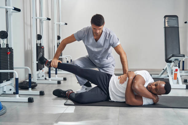 Qualified focused physical therapist checking strength of young male patient leg muscles