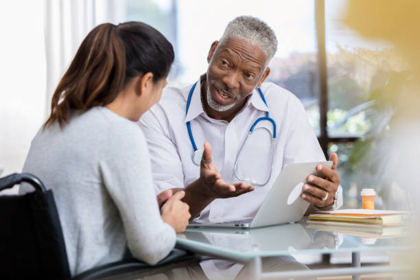 Male doctor gestures while taking to female patient. The patient is sitting in a wheelchair.